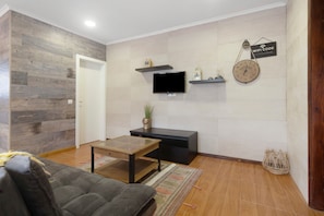 Una sala de estar con un sofá, una mesa de centro, un televisor, un reloj y una estantería con objetos decorativos.
