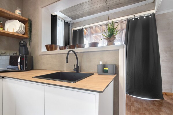 A kitchen with a black sink, wooden countertop, and a window with a plant and curtains.