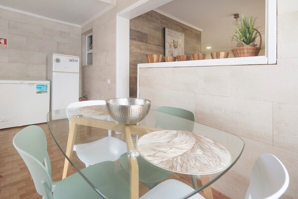 Una cocina moderna con una mesa de comedor de vidrio, sillas blancas, un refrigerador y un mueble de madera con una planta.