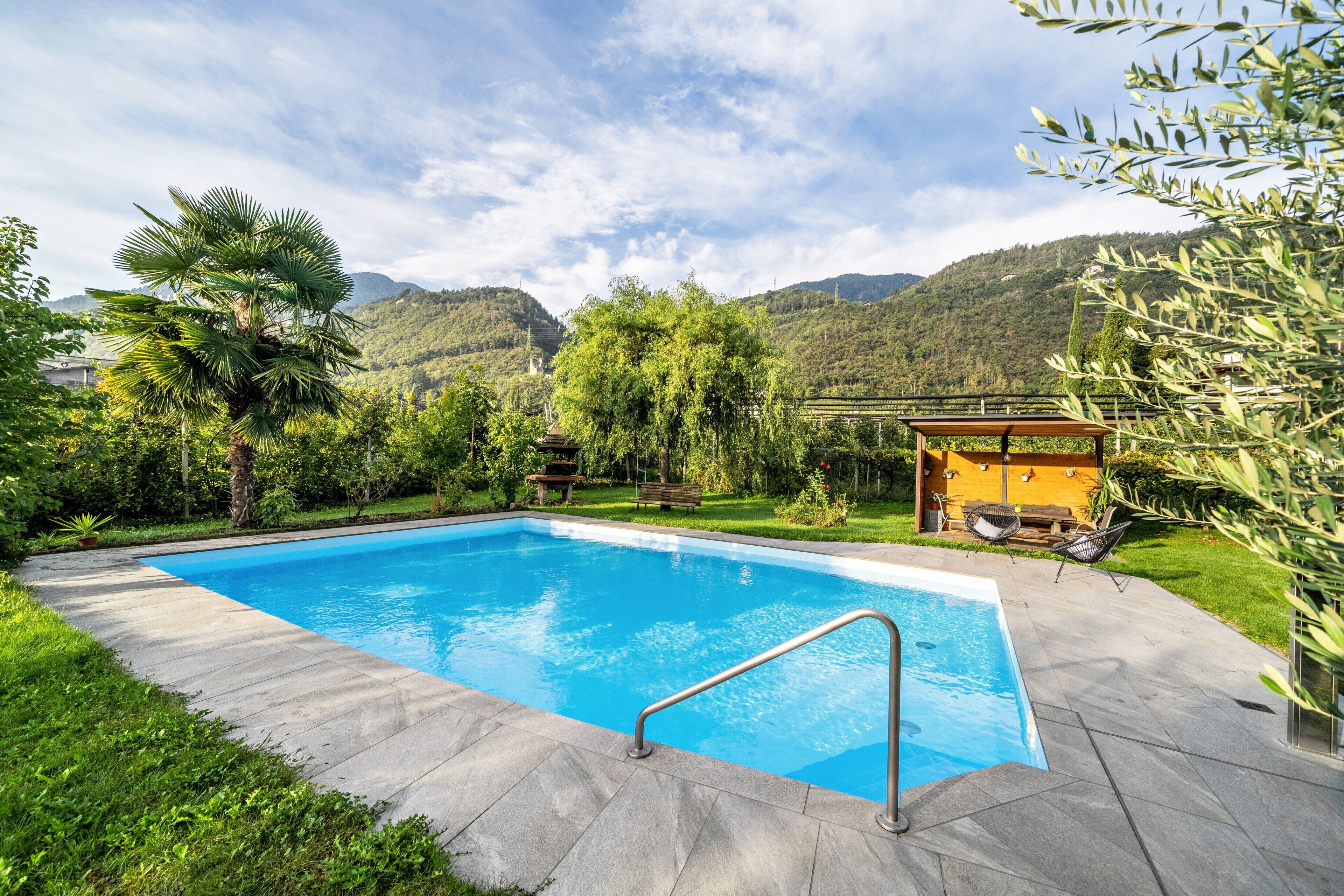 A rectangular swimming pool with a metal safety rail, surrounded by a stone deck.