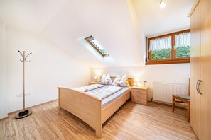 Ein Schlafzimmer mit Dachfenster, Holzboden, einem Bett mit Blumenmuster, Nachttischlampen, einem Nachttisch, einem Sessel und einem Kleiderschrank.