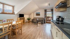 A modern kitchen with wooden cabinets, a dining area with a table and chairs, a sofa, and a TV in a loft bedroom. - Holiday Apartment 'Erlengut Burgstall' with Mountain View, Shared Pool and Wi-Fi (Lana)