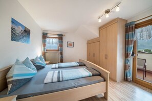 Un dormitorio con cama, ventana con cortinas, radiador y vistas al exterior.