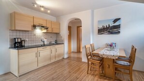 A modern kitchen with wooden cabinets, a coffee maker, and a dining area with a table and chairs. - Holiday Apartment 'Erlengut Burgstall' with Mountain View, Shared Pool and Wi-Fi (Lana)