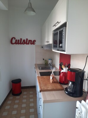 A kitchen with a microwave, sink, and a red kettle on the counter.