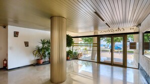 Een moderne lobby met een grote kolom, potplanten en een glazen deur naar buiten.