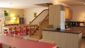 A modern kitchen with wooden cabinets, a central island, and a dining area with red chairs and a red table.