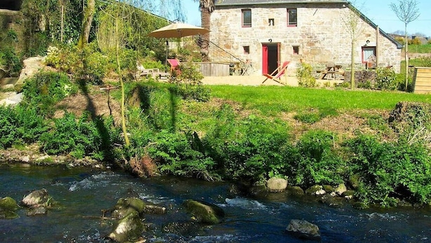 A stone house with a red door, a small garden, and a stream in front.