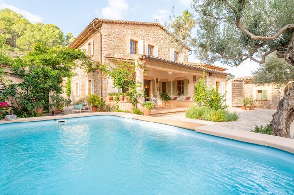 A stone villa with a swimming pool, surrounded by greenery and trees.