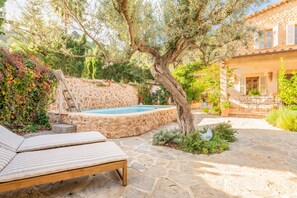 Una piscina de piedra, sillones de descanso y un rústico muro de piedra.