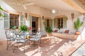 A sunlit patio with a round table and chairs, potted plants, and a stone wall.