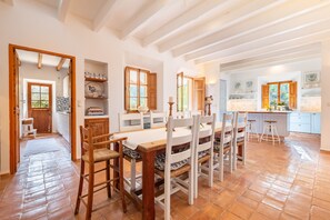 A spacious kitchen with wooden beams, a dining area with white chairs, and a view of the garden.