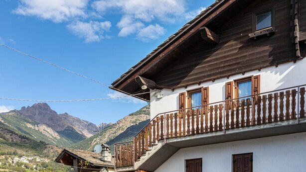 A two-story building with a balcony, a mountain backdrop, and a clear sky. - Lo Sondzo Holiday Home – Your Dream Stay in Valle d'Aosta (Nus)