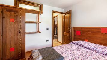 Ein Schlafzimmer mit einem hölzernen Kopfteil, einem Bett mit gemusterten Betttextilien, einem Holzschrank und einem kleinen Hocker.