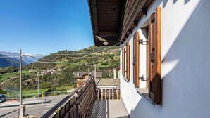 A balcony with a view of a mountainous landscape, a wooden railing, and a building with wooden shutters. - Lo Sondzo Holiday Home – Your Dream Stay in Valle d'Aosta (Nus)