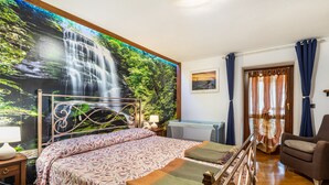 A bedroom with a bed, a chair, a nightstand, a lamp, a window with curtains, and a wall mural of a waterfall. - Lo Sondzo Holiday Home – Your Dream Stay in Valle d'Aosta (Nus)
