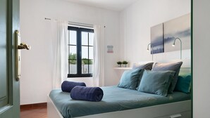 A bedroom with a bed, a window with curtains, a bedside table with a lamp, and a wall-mounted artwork. - Vacation Home 'Casa Jess' with Private Terrace, Private Garden and Wi-Fi (Tías)