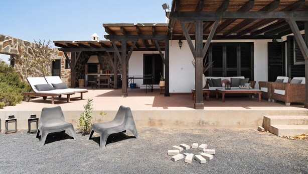 A covered outdoor seating area with lounge chairs and a table, a pergola structure, and a stone wall. - Vacation Home 'Casa Jess' with Private Terrace, Private Garden and Wi-Fi (Tías)