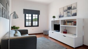 A modern living room with a sofa, a TV, a white entertainment unit, and artwork on the wall. - Vacation Home 'Casa Jess' with Private Terrace, Private Garden and Wi-Fi (Tías)