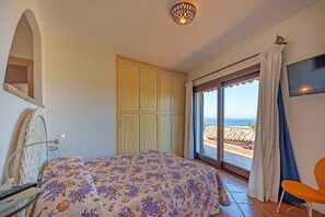 Une chambre à coucher comprenant un lit, un bureau avec un ordinateur, une chaise, une armoire et un balcon avec vue sur la mer.