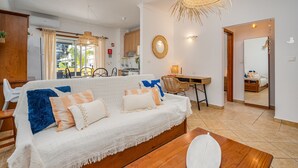 A living room with a sofa, a dining table, and a kitchen in the background. - Apartment 'Joana' with Shared Pool, Wi-Fi and Air Conditioning (Portimão)