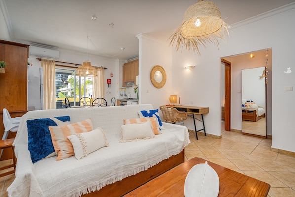 A living room with a sofa, a dining table, and a kitchen in the background.