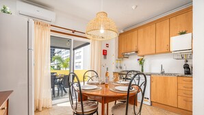 A kitchen with wooden cabinets, a dining table with chairs, and a hanging light fixture. - Apartment 'Joana' with Shared Pool, Wi-Fi and Air Conditioning (Portimão)