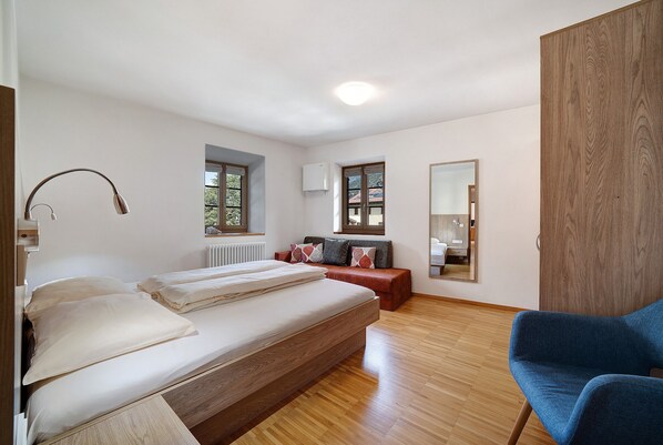 Un dormitorio con cama, lámpara de noche, ventana, radiador, espejo y armario.