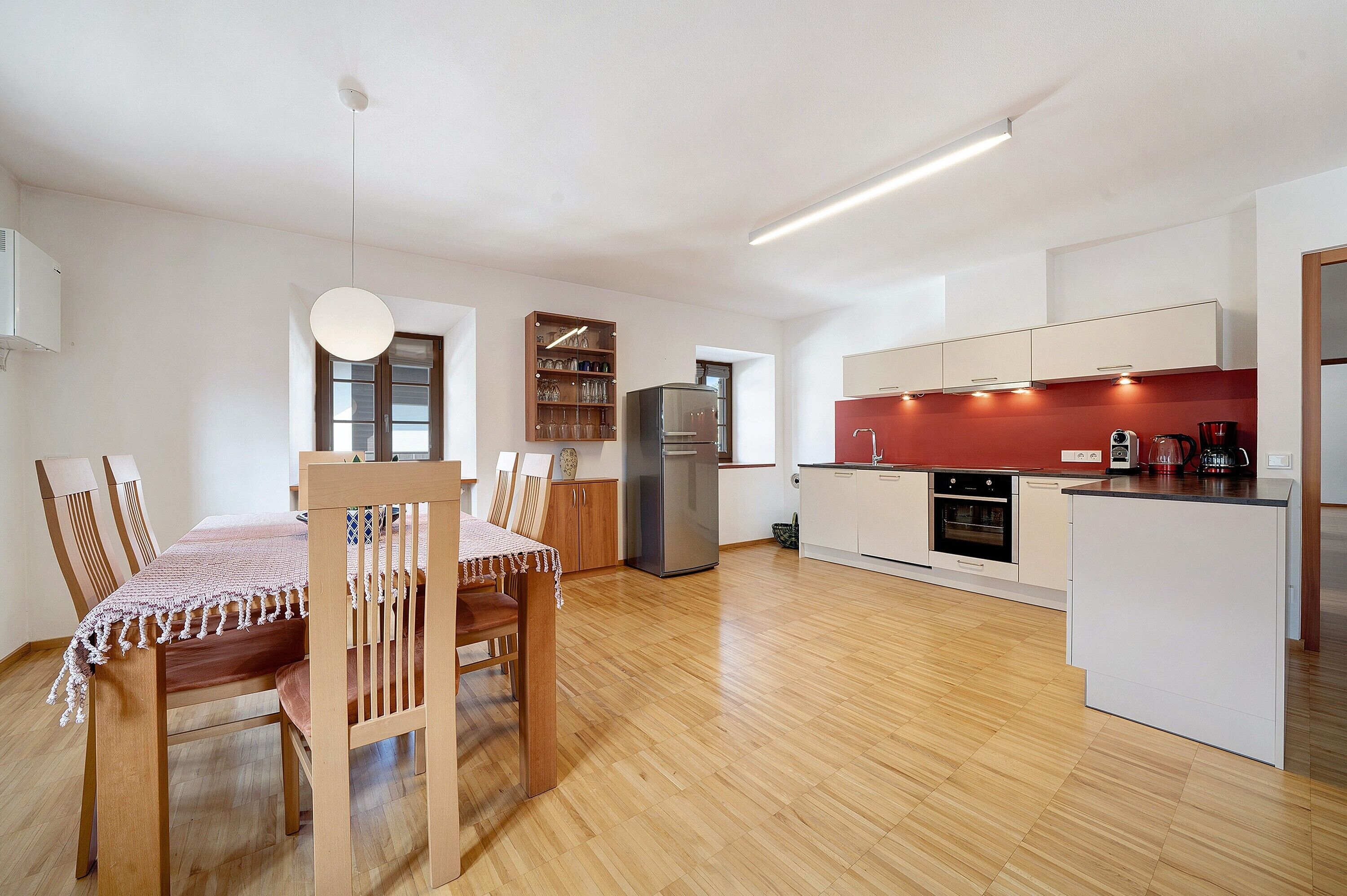 A modern kitchen with white cabinets, a refrigerator, and a dining area with a wooden table and chairs.