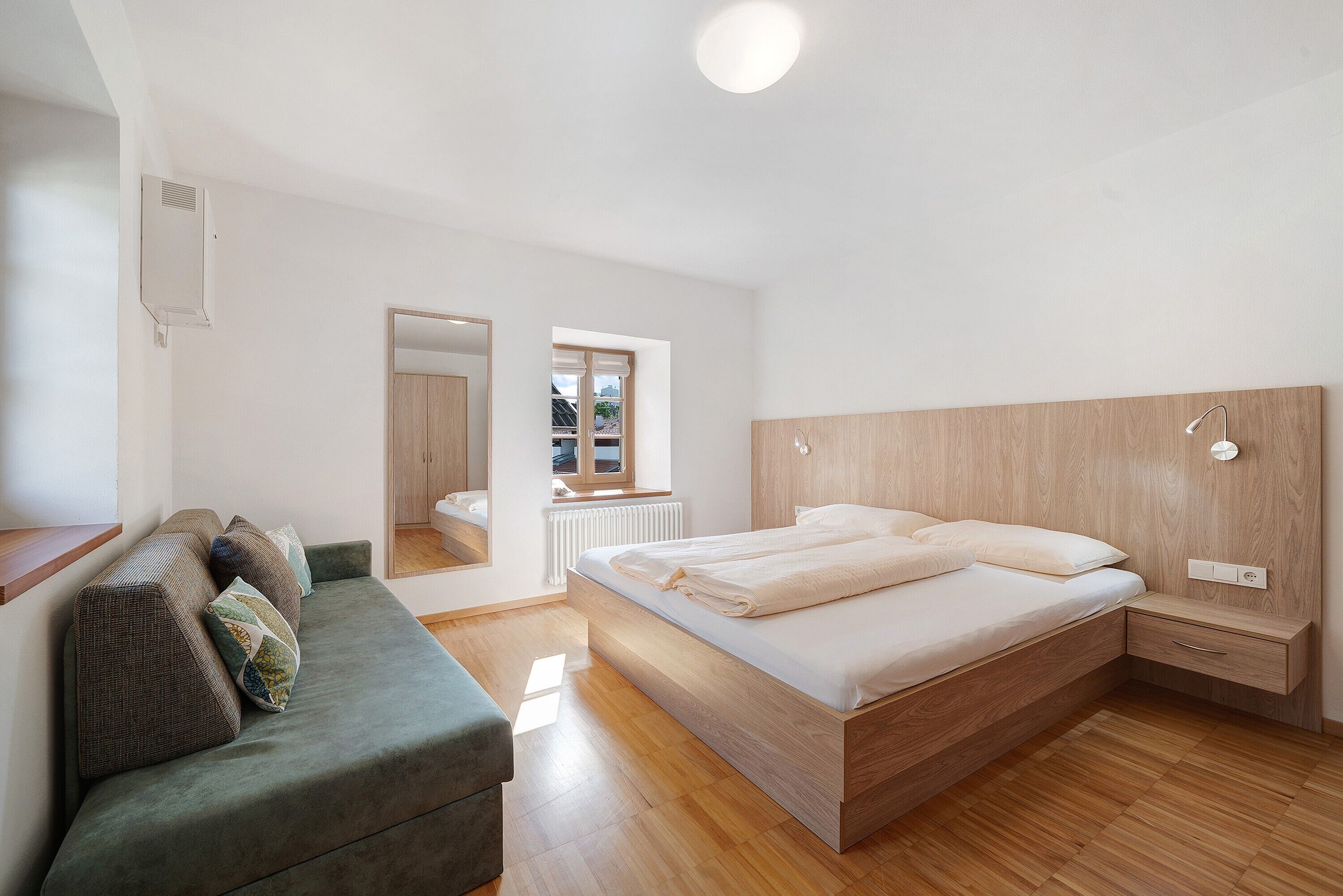 Une chambre à coucher comprenant un lit, un canapé, une tête de lit en bois, une table de chevet et une fenêtre.