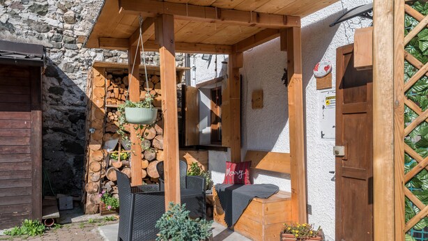 Un espace extérieur aménagé avec des sièges en bois, un mur en pierre, une porte en bois et une plante suspendue.