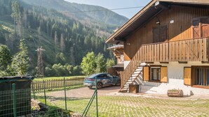 Un bâtiment en bois doté d’un balcon, une voiture garée devant, et un paysage montagneux en arrière-plan.