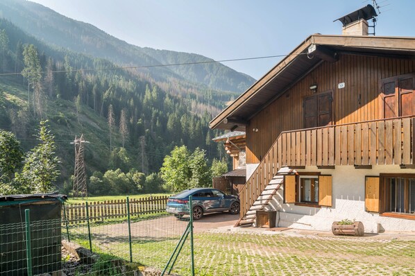 Un bâtiment en bois doté d’un balcon, une voiture garée devant, et un paysage montagneux en arrière-plan.