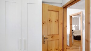 Un couloir avec une porte en bois, des murs blancs et un lit visible au fond.