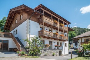 Un immeuble à plusieurs étages doté de balcons en bois, d’un mur en pierre et d’un escalier menant à l’entrée.