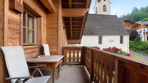 A wooden balcony with a table and chairs, a view of a church, and a white building with a sign.