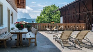 A patio with wooden benches and tables, a wooden fence, and a view of mountains.