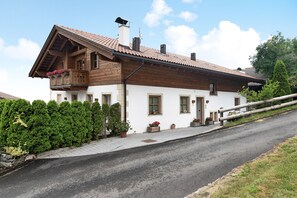 A two-story house with a sloped roof, wooden balcony, and potted plants.