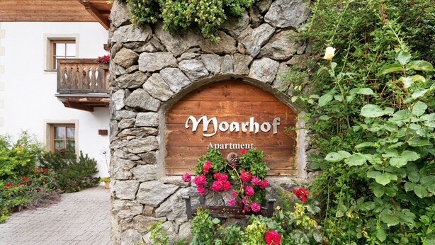 A stone wall with a wooden sign reading 'Moarhof Apartment.'