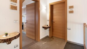 A hallway with wooden doors, a wooden wall-mounted shelf, and a small sink with a plant.