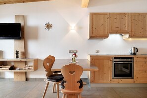 A kitchen with wooden cabinets, a built-in oven, a TV mounted on the wall, and a dining table with chairs.