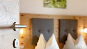 A wooden door with a keyhole and a lock, a bed with white bedding and a headboard with a tufted design, and a painting on the wall.