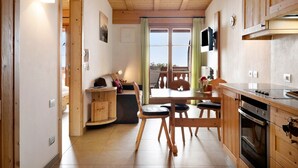 A compact kitchen with wooden cabinets, a dining area with a table and chairs, and a view through a window.
