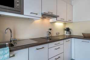 Uma cozinha moderna com uma pia de aço inoxidável, chaleira, máquina de café e micro-ondas.