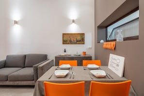 A dining area with a table set for four, a grey sofa, and a painting on the wall.
