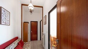 A hallway with a wooden door, a radiator, a sofa with red cushions, and a dining table with chairs. - Apartment 'Casa Cogoleto Terrace and Parking' with Sea View, Wi-Fi and Air Conditioning (Cogoleto)