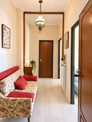 A hallway with a wooden door, a red sofa with floral upholstery, a hanging light fixture, and a radiator. - Apartment 'Casa Cogoleto Terrace and Parking' with Sea View, Wi-Fi and Air Conditioning (Cogoleto)