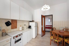 Una cucina con mobili bianchi, un fornello e un'area pranzo con tavolo e sedie in legno.