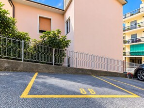 Une place de stationnement marquée du numéro « 8B » sur une surface goudronnée, située à côté d’un bâtiment entouré d’une clôture en métal et agrémenté de verdure.