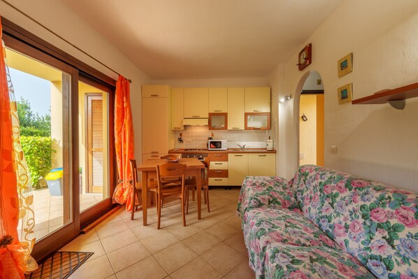 A compact kitchen with a dining area, a sofa, and a view through a sliding door.
